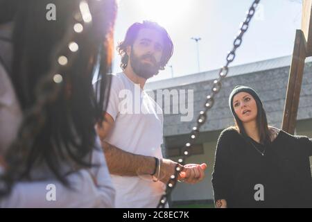 Young man talking with female friends while standing against clear sky on sunny day Stock Photo