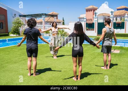 Young woman teaching yoga to friends at back yard on sunny day Stock Photo
