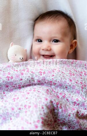 Portrait of happy baby girl lying on bed with teether Stock Photo
