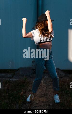 Female hip-hop dancer dancing against wall during sunny day Stock Photo
