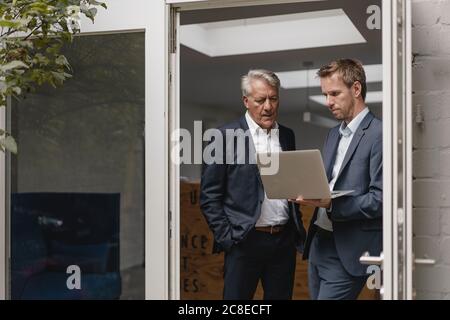 Two confident businessmen using laptop, standing in office door Stock Photo