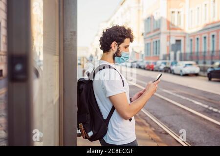 Man with backpack wearing mask while using mobile phone in city Stock Photo
