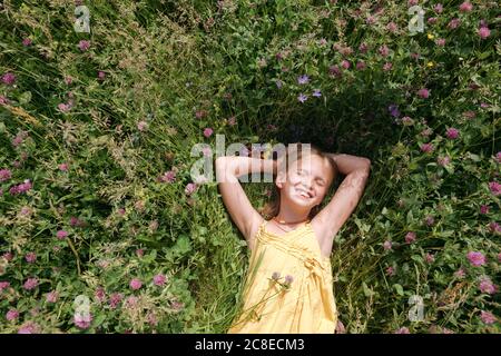 Portrait of happy little girl with eyes closed lying on a meadow in summer Stock Photo