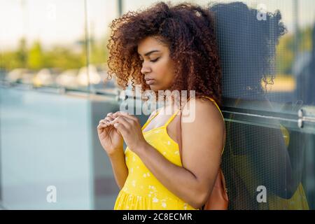 Young woman with afro hair wearing yellow dress standing by modern wall in city Stock Photo