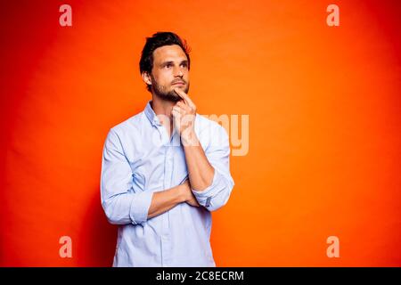 Thoughtful handsome man looking away while touching chin against orange background Stock Photo