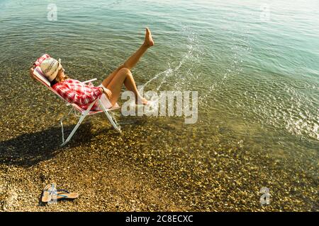 Young woman sitting on deckchair in river splashing with water Stock Photo