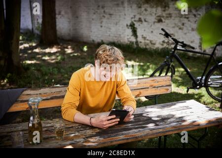 Laughing young man sitting at beer table in garden using digital tablet Stock Photo