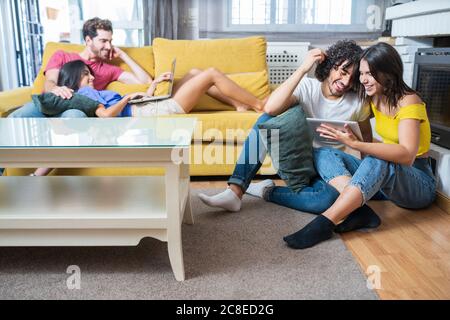 Happy young couples using technologies while sitting in living room Stock Photo