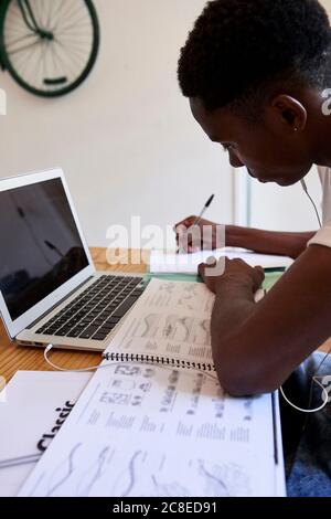 Focused young man writing notes in book while sitting at home Stock Photo