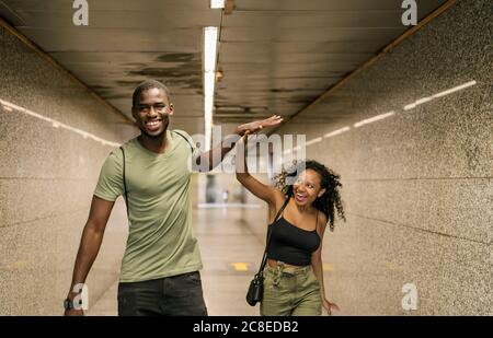 Cheerful couple giving high-five while walking in underground walkway at subway station Stock Photo