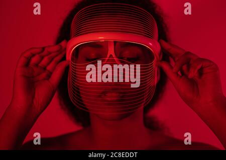 Close-up of young woman wearing red led mask against wall at home Stock Photo