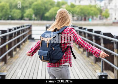 Happy woman wearing checked shirt with backpack spinning on bridge Stock Photo