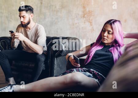 Young man and woman sitting on sofa and armchair in a loft using smartphones Stock Photo