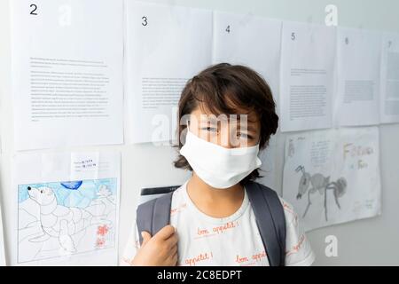 Close-up of boy wearing mask standing against papers stuck on wall in school Stock Photo