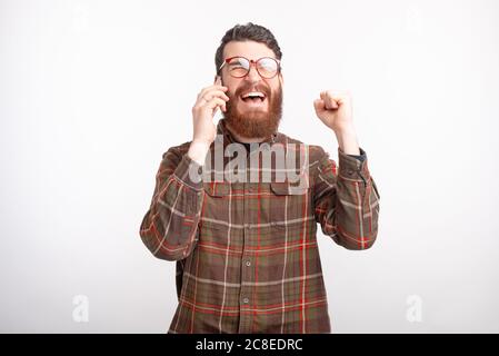 Bearded man wearing glasses is talking on the phone hears some good news makes the winner gesture. Stock Photo