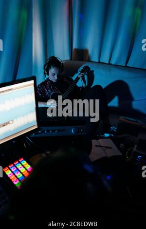 Woman playing guitar while man using computer in recording studio at home Stock Photo