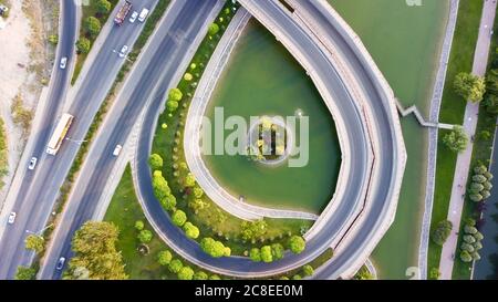 Aerial view of the roundabout on the river. Trees, overpass, buildings and vehicles can be seen. Stock Photo