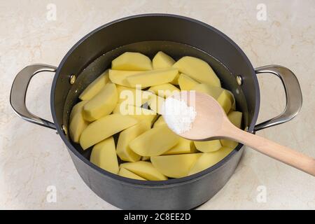 Add salt to a saucepan with raw peeled potatoes cut into quarters and ready to boil. Cook at home delicious vegetable dish. Vegetarian food. Stock Photo