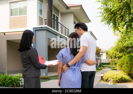 Asian woman Real estate broker agent showing a house detail in her file to the young Asian couple lover looking and interest to buy it. Buying a new h Stock Photo