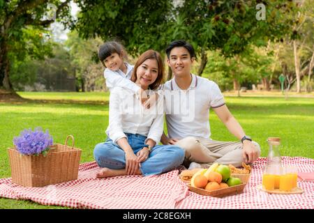 Asian teen family happy holiday picnic moment in the park with father, mother and daughter looking at camera and smile to happy spend vacation time to Stock Photo