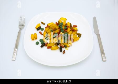 Many different weight loss pills and supplements as food on white plate with fork and knife. Diet pills and supplements, prescription weight loss drug Stock Photo