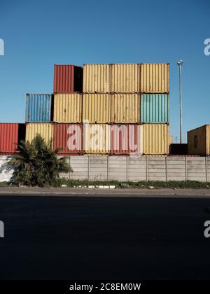 Colourful containers stacked next to a busy street in an industrial part of town. No people. Stock Photo