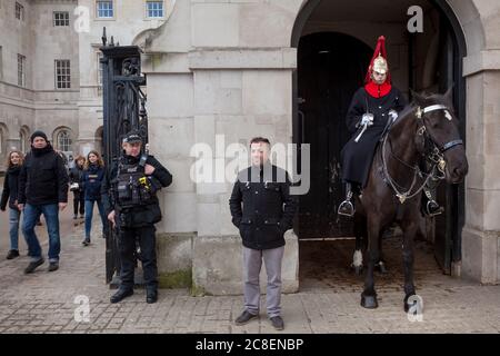 Tourist poses for photographs in front of a mounted soldier from the Household Cavalry and a heavily armed police officer at  Horse Guards, London UK Stock Photo