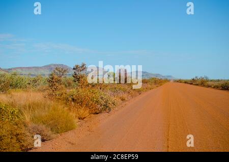 Dirt gravel road in remote outback Australia, with mountain range of Hamersley or Karijini National Park in the Pilbara, Western Australia, in the bac Stock Photo