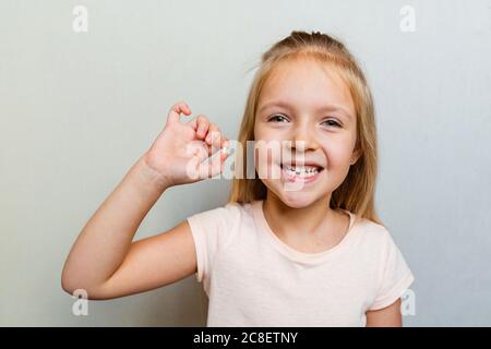 Kid showing the first milk tooth. Change teeth concept. Cute little girl with blonde hair on gray background with copy space. Stock Photo