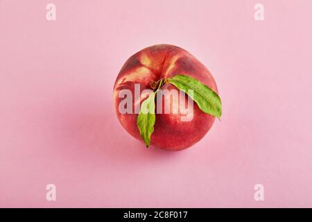 Fresh juicy peach with green leaves isolated on a pink background. Flat lay Stock Photo