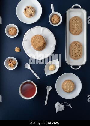 Different types of cookies on white plates and cup of tea on dark blue background. Overhead shot. Stock Photo