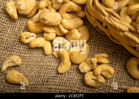 Cashew nuts in a wicker basket and cashew nuts scattered on burlap with a rough texture surface texture. Close up Stock Photo