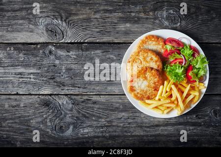 fried turkey burgers served with lettuce tomato salad and french fries on a white plate on a rustic wooden table, horizontal view from above, flatlay, Stock Photo