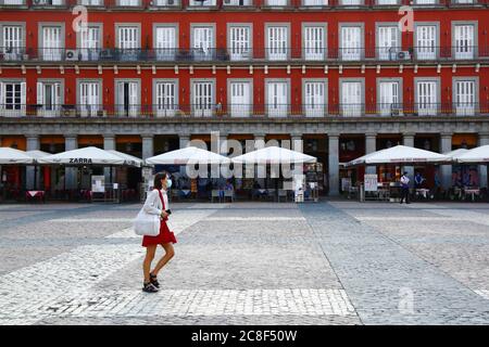 23rd July 2020, Plaza Mayor, Madrid, Spain: A woman wearing a face mask walks across a near empty Plaza Mayor / Great Square. Since June 21st Spain has relaxed travel restrictions after a strict lockdown to control the Covid 19 coronavirus. Spain is one of the world's most visited countries and tourism an important contributor to the Spanish economy. The Plaza Mayor is one of Madrid's main attractions and would normally be full of people and tourists at this time of year. Stock Photo