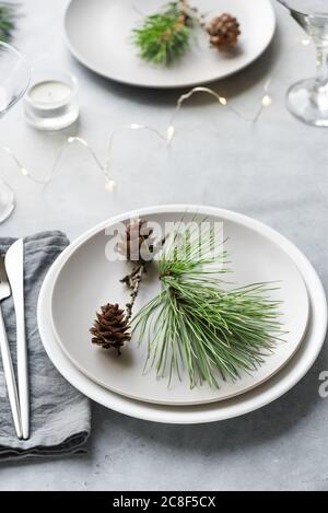Christmas Table Setting with pine branches and cones on light grey table, copy space. Christmas dinner, party design, concept. Stock Photo