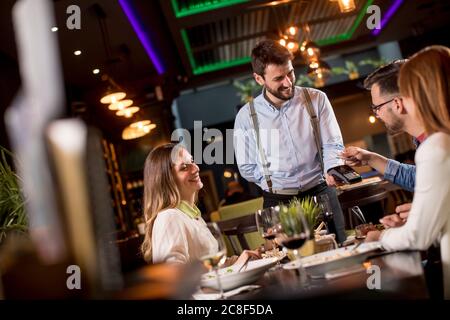 Young man paying with contactless credit card in the restaurant after dinner Stock Photo