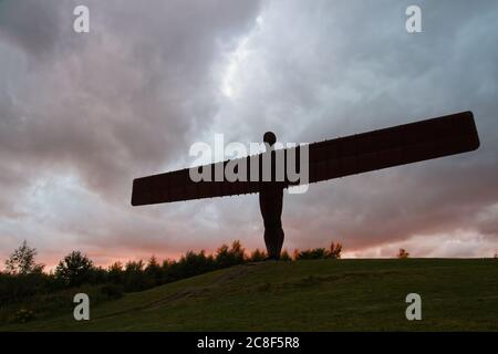 The iconic iron statue of The Angel of the North designed by Anthony Gormley standing proudly in silhouette against a dramtic cloud filled sky at suns