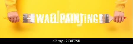 Paint brush in hand over yellow background, wall painting concept, panoramic image