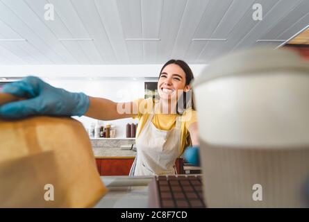 Bar owner working only with take away orders during corona virus outbreak - Young woman worker wearing surgical gloves giving takeout meal to customer Stock Photo