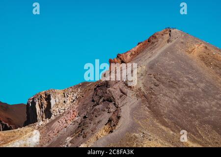 Hikers prepare to descend down a ridge on the Tongariro Alpine Crossing, a popular day walk in New Zealand Stock Photo