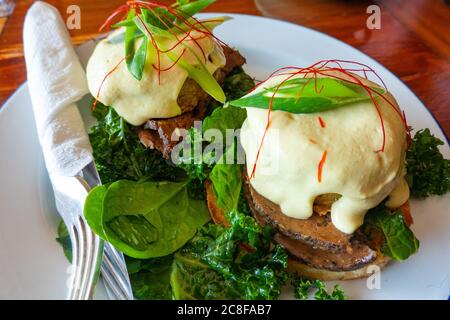 A vegan benedict breakfast - mock meat, hash brown and hollandaise sauce served on kale and an English muffin, at a plant-based restaurant Stock Photo