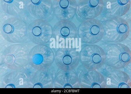 Horizontal color image with an overhead view of an empty clear plastic bottles with caps stacked on a blue background. Recycling and environment conce Stock Photo