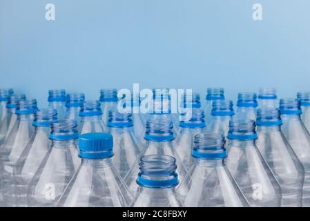 Horizontal color image with a front view of an empty clear plastic bottles with caps stacked on a blue background. Recycling and environment concept. Stock Photo