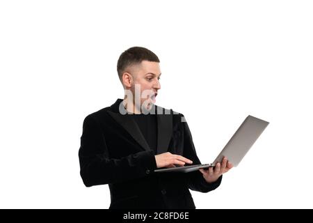 A shocked man holds a laptop in his hands and looks at him with surprise with his mouth open and big eyes. Isolated Stock Photo
