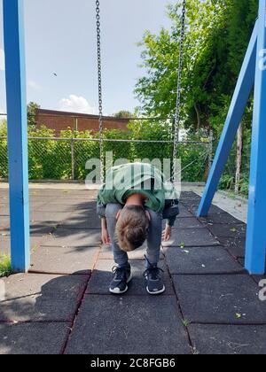 boy sitting listlessly on a swing and has his head hanging, Germany Stock Photo