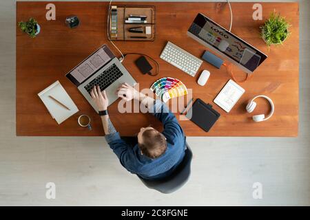 Directly above view of man with tattoo sitting at wooden table and editing ui design on laptop Stock Photo