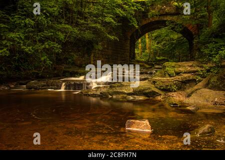 Small red brick bridge over the stream at falling foss waterfall Stock Photo