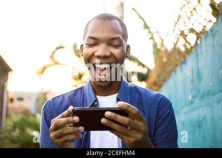 Shallow focus of a cheerful African American male watching a video on his phone under the sunlight Stock Photo