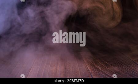 Conceptual image of multi-colored smoke isolated on dark black background and wooden table. Stock Photo
