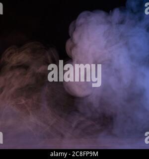 Conceptual image of multi-colored smoke isolated on dark black background and wooden table. Stock Photo